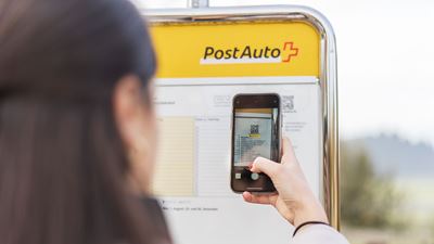 A woman scans a QR code on the timetable at the bus stop using her smartphone.