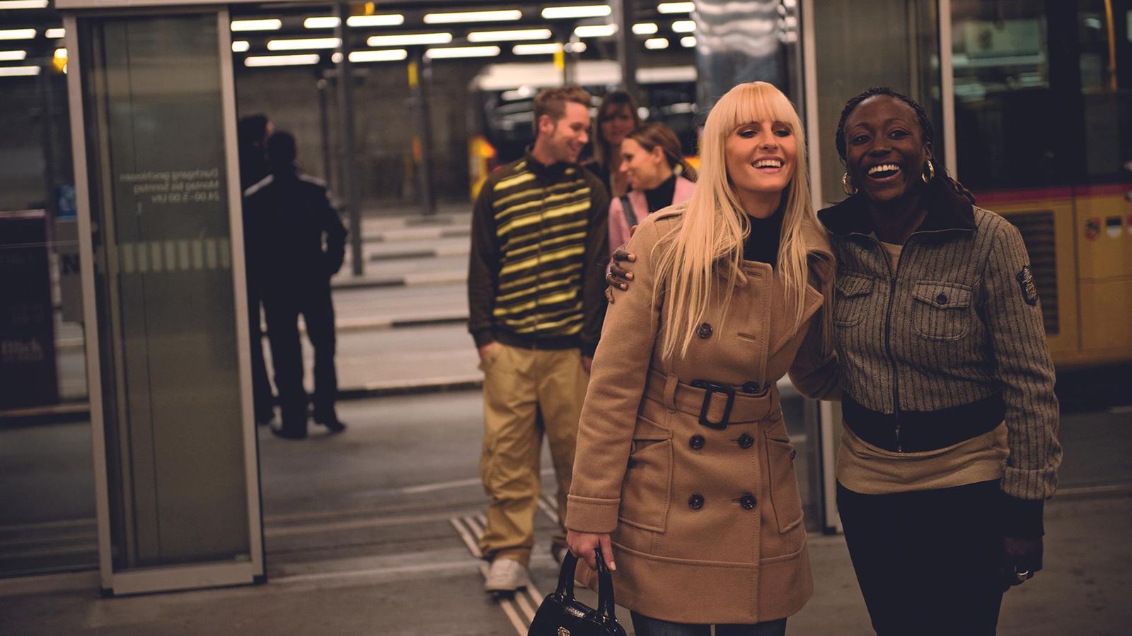 Two women laughing at the PostBus station
