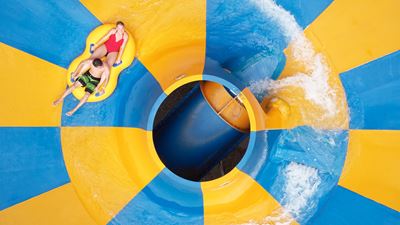 Two visitors slide on a blue and yellow water slide with a rubber ring © Alpamare | Bad Seedam AG