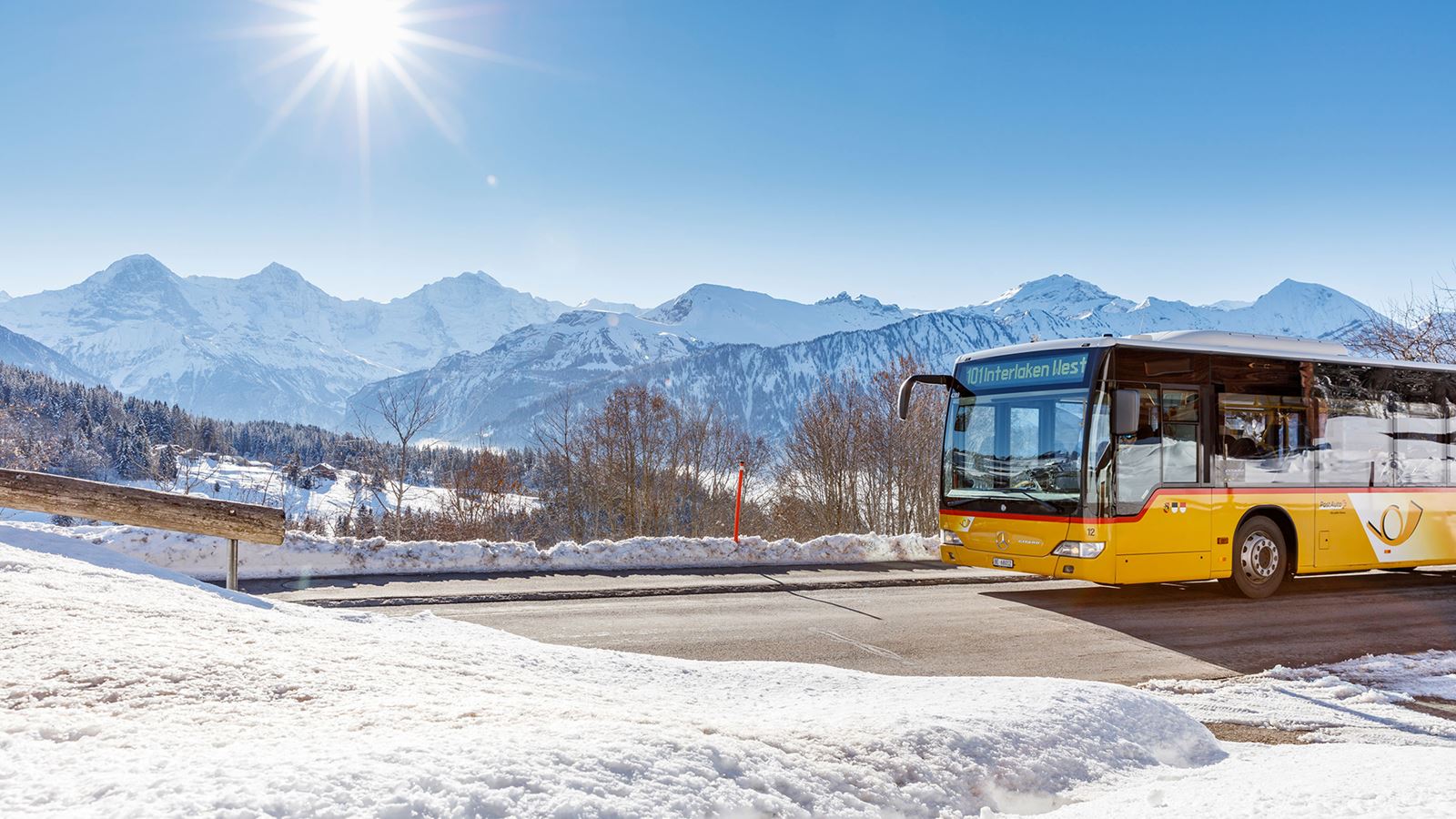 A Postbus travels towards Interlaken. The snow-covered mountains can be seen in the background.