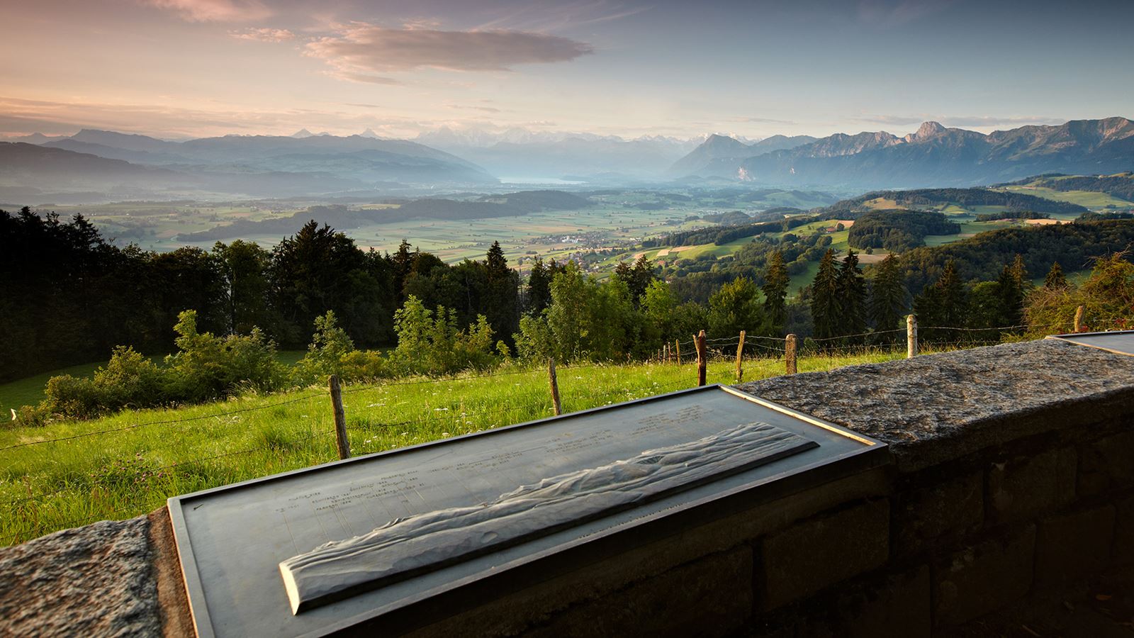 In primo piano un cartello con informazioni sulla catena montuosa nello sfondo. Vista sulla catena del Gantrisch e sul Lago di Thun.