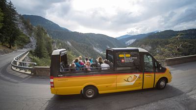 A PostBus cabriolet drives through the imposing Rhine Gorge.