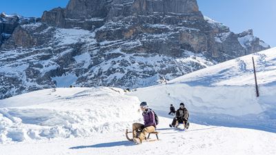 Drei Schlittenfahrer hintereinander auf Davoser Schlitteln vor schroffer Felswand sausen Richtung Schwarzwaldalp.