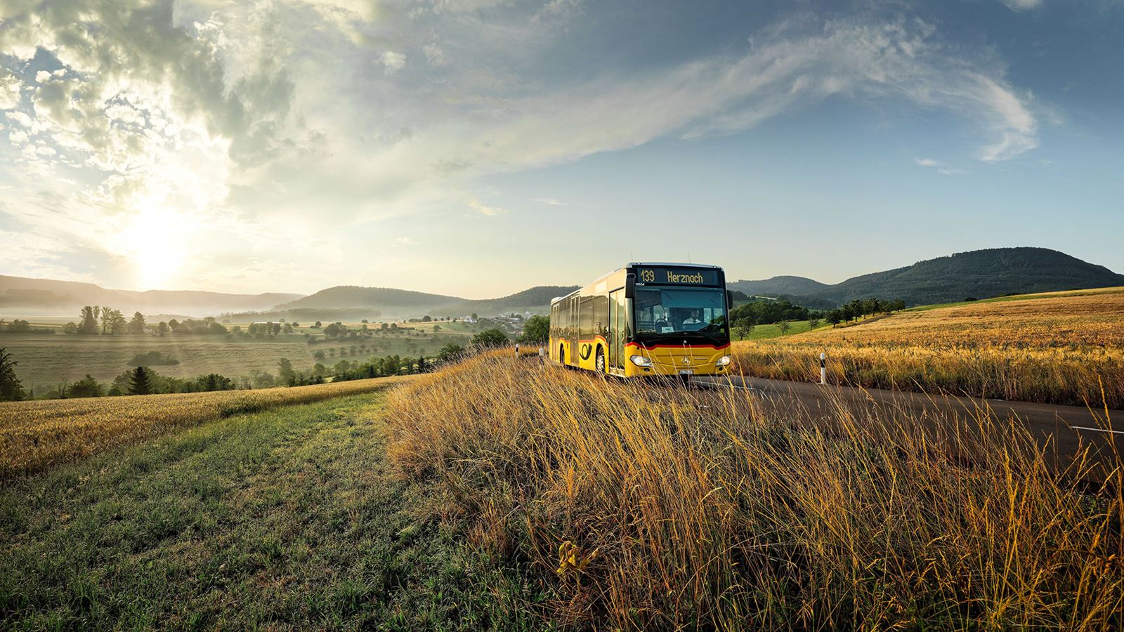 Postauto in hügeliger Landschaft im Gegenlicht