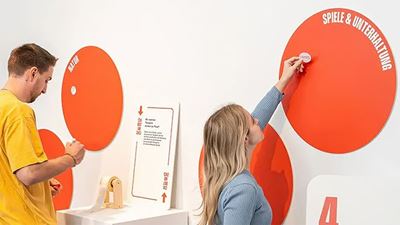 Zwei Personen platzieren Begriffe auf großen orangefarbenen Themenkreisen an einer interaktiven Wand.