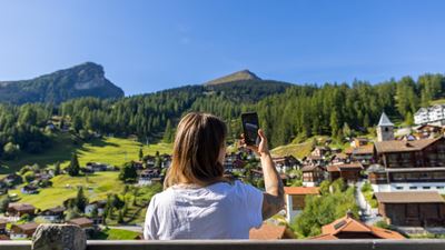 An overnight guest photographing a Swiss mountain landscape with their smartphone – on the go with the guest card.