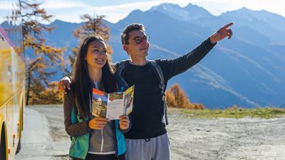 A man and a woman stand in front of a PostBus and plan their way.