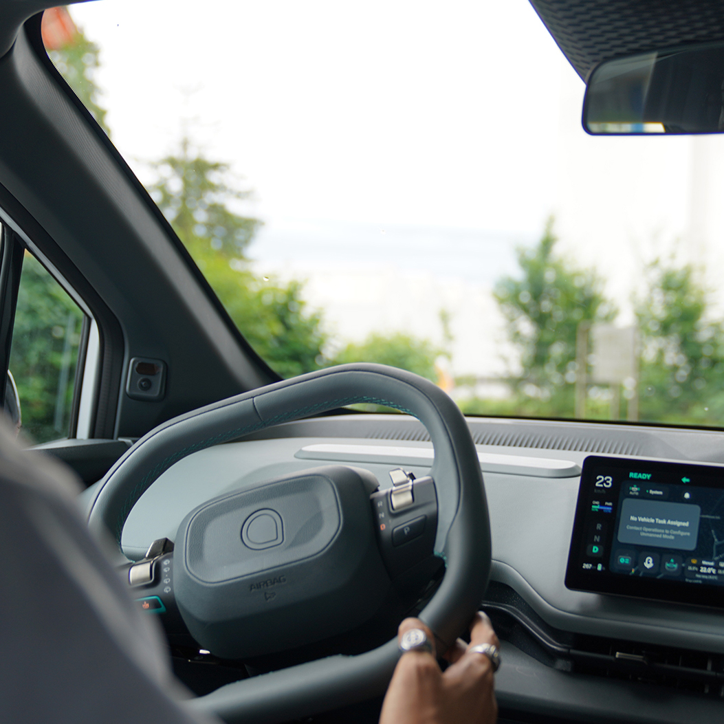 Une personne est assise au volant d’une voiture moderne; un système de navigation est visible sur l’écran.