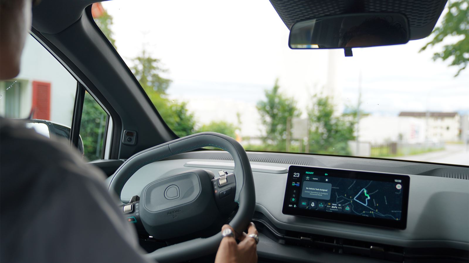 Person sitzt am Steuer eines modernen Autos; auf dem Display ist ein Navigationssystem zu sehen