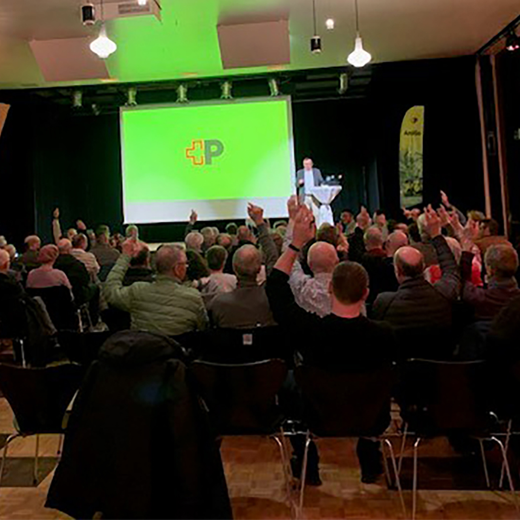 Manifestation destinée à la population dans la salle communale. Présentation d’AmiGo devant un écran avec le logo de la Poste.