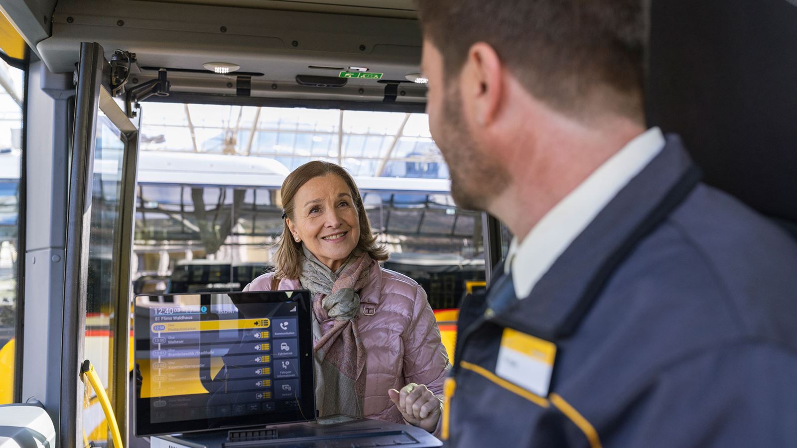 A woman boards a Postbus and receives a friendly greeting from the driver.