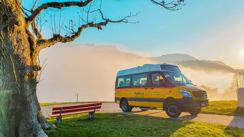 Ein Postauto Kleinbus mit der Aufschrift PubliCar auf einem Hügel. 