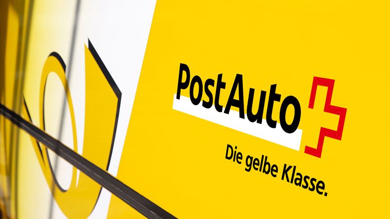A close-up of a Postbus that shows the company name, the post horn and the claim “The yellow class”. 