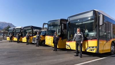 Six Postbuses lined up next to one another. In front of every Postbus is a driver in a PostBus uniform. 