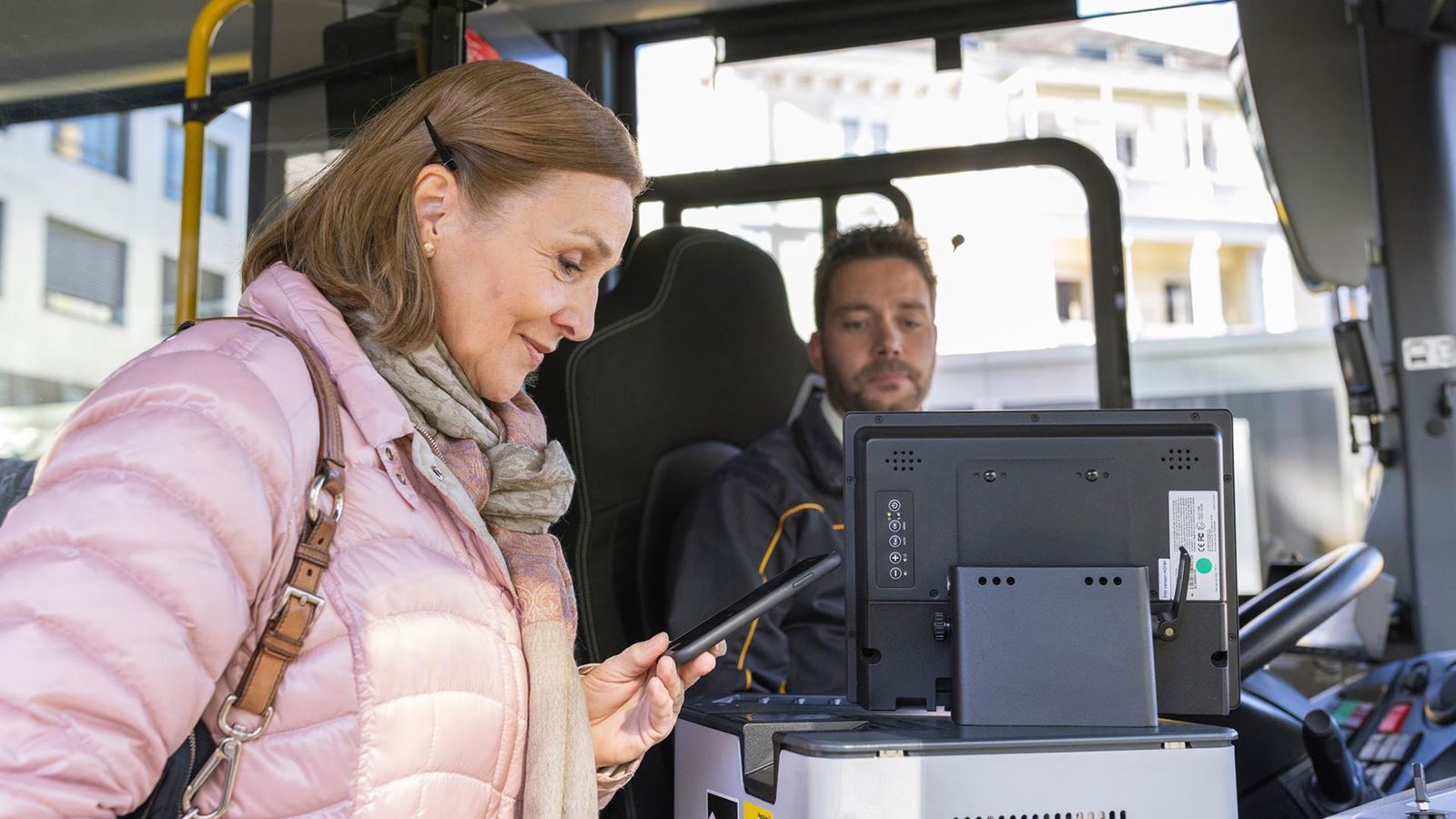 A woman buys her ticket when she boards the Postbus and looks at her smartphone.