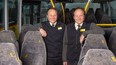 Fluri (links) und Dägi Aebli stehen nebeneinander in der Fahrer-Uniform in einem Postauto in Chur
